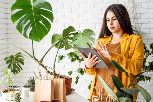 Home gardening. Small business. Young woman gardener making notes in the notepad, line of craft shopping bags for packing plant in the front