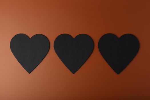Minimalistic flat lay with three black hearts on brown background. Concept of love and relationship. High quality photo