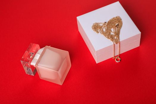 A gift for Valentine's Day. Perfume and a box with a gold chain on a red background.