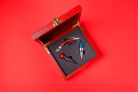 Gift set of corkscrew and removable lids. Wine corks and bottle openers in a wooden box on a red background.