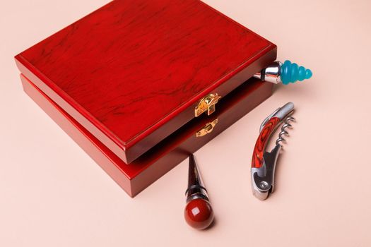 Gift set of corkscrew and removable lids. Wine corks and bottle openers in a wooden box on a pink background.
