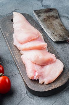 Pieces of raw and uncooked chicken fillets, on gray background