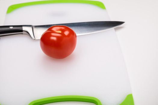 A fresh red tomato and a large chef's knife lie on a cutting board. On an isolated white background.