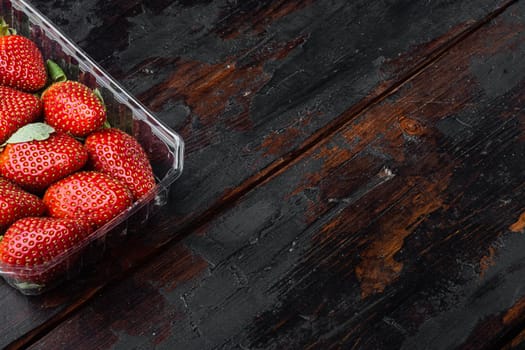Red ripe strawberrie in clear plastic tray, on old dark wooden table background with copy space for text
