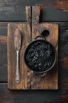 Black bowl of black caviar, on old dark wooden table background, top view flat lay