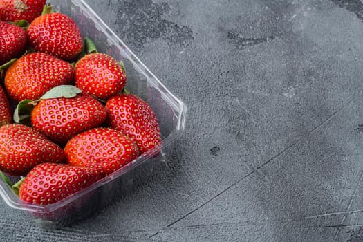 Red ripe strawberrie in clear plastic tray, on gray background with copy space for text