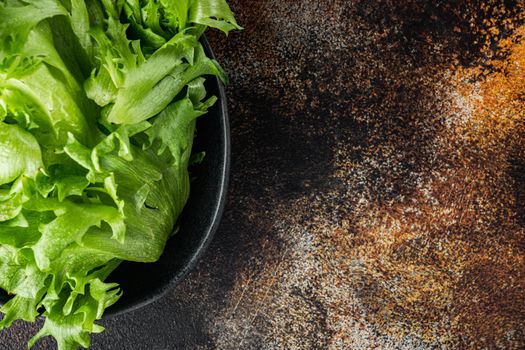Raw organic green oak lettuce leaves, on old dark rustic background, top view flat lay with copy space for text