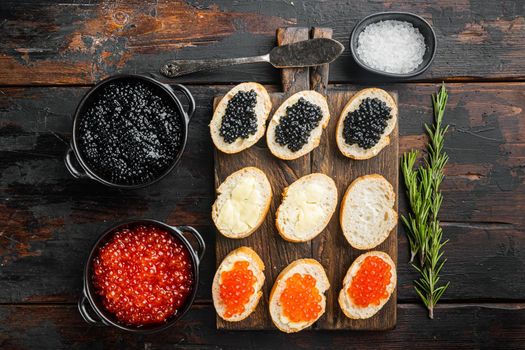 Bruschettes with butter red, and black caviar, on old dark wooden table background, top view flat lay