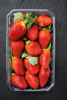 Transparent plastic tray, with freshly picked strawberries, on black background, top view flat lay
