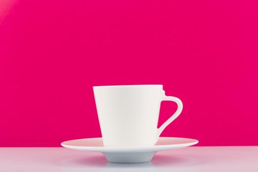 Minimalistic still life with white shiny ceramic coffee cup with saucer against pink background with copy space. High quality photo