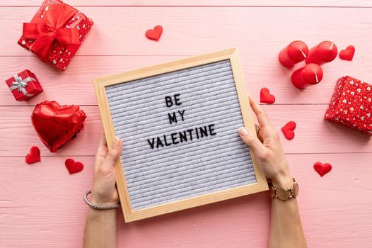 Valentines Day. Top view female hands holding felt letter boead with text Be My Valentine on pink wooden background