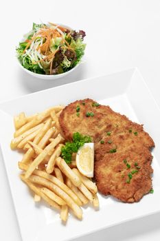 german breaded pork schnitzel with french fries on white studio background