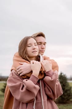 Happy young loving couple wearing hoods embracing each other outdoors in the park