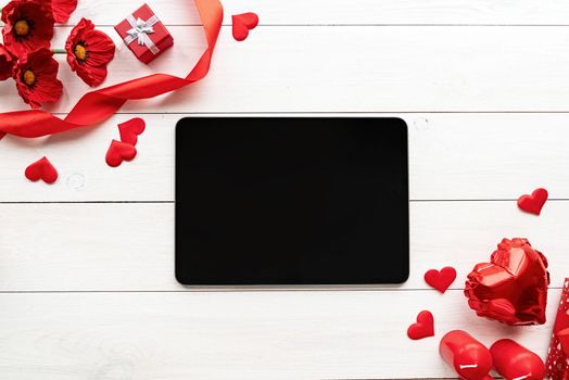 Valentines Day. Tablet with black screen with valentine decorations candles, balloons and confetti top view on white wooden background