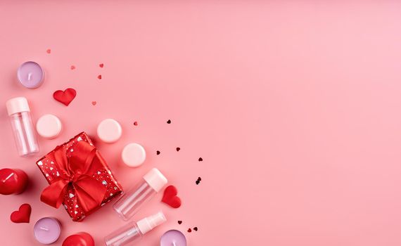 Valentines Day and Womens Day concept. Fashion cosmetic accessories with gift box, empty tubes and bottles, candles and confetti top view flat lay on pink background with copy space