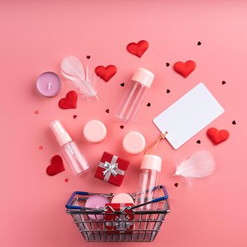 Valentines day shopping. Shopping basket with various cosmetics, price tag, confetti top view flat lay on pink background