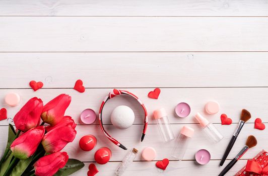 Valentines Day and Womens Day concept. Fashion cosmetic accessories with gift box, empty tubes and bottles, candles and confetti top view flat lay on white wooden background with copy space