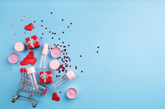 Valentines day shopping. Shopping basket with various cosmetics, price tag, confetti top view flat lay on blue background