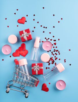 Valentines day shopping. Shopping basket with various cosmetics, price tag, confetti top view flat lay on blue background