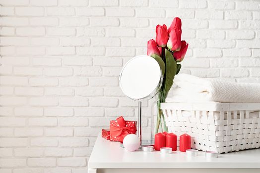 Valentines Day and Womens Day concept. cosmetic and spa accessories with gift box, flowers and candles front view on white brick wall background with copy space