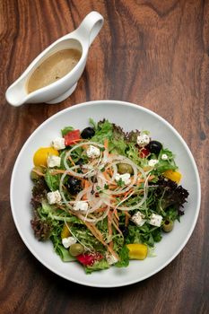 greek salad with feta cheese and olives with citrus vinaigrette on wooden table