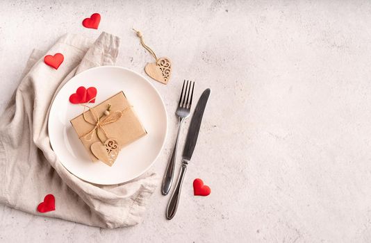 Valentines Day and Womens Day concept. Valentines day table setting with an eco gift box, hearts, fork and knife top view with copy space