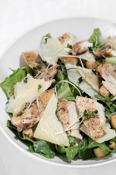 organic chicken caesar salad with parmesan cheese and croutons on white table background