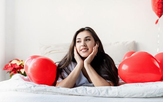 Valentine's Day. Sleeping. Young happy brunette woman laying in the bed with red heart shaped balloons