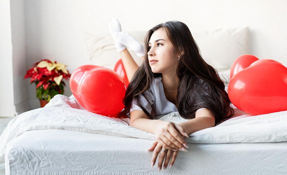 Valentine's Day. Sleeping. Young happy brunette woman laying in the bed with red heart shaped balloons