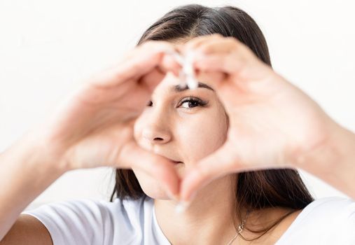 Valentine's Day. Young happy brunette woman in white t-shirt showing heart sign with her hands in front of face