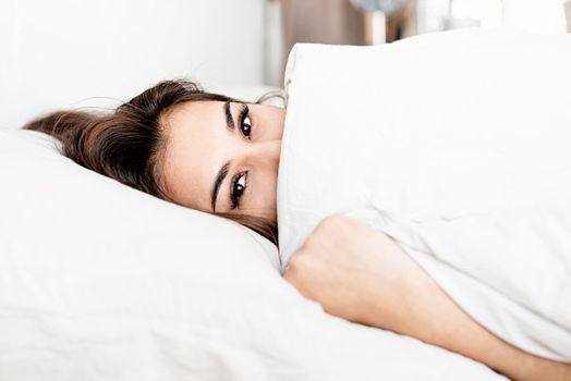 young beautiful brunette woman sleeping in bed covering her face with blanket