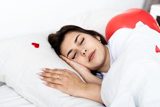 Valentines Day. Young brunette woman sleeping in the bed with red heart shaped balloons and decorations