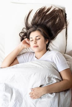 young beautiful brunette woman sleeping in bed covering her face with blanket