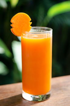 glass of fresh organic carrot juice on table outdoors on table in sunny garden outdoors