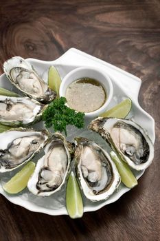 Six fresh oysters with lime wedges and citrus vinaigrette sauce