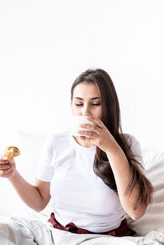 Breakfast and morning routine. Young brunette woman sitting in the bed with eating croissants