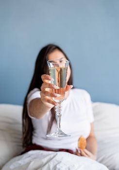 Valentines Day. Young brunette woman sitting awake in the bed with red heart shaped balloons and decorations drinking champagne eating croissants