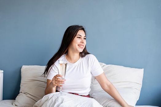 Valentines Day. Young brunette woman sitting awake in the bed drinking champagne