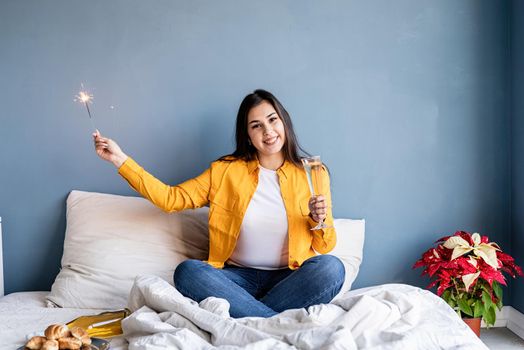 Valentines Day. Young brunette woman sitting in the bed drinking champagne holding a sparkler