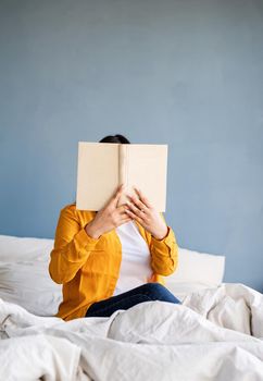 Breakfast and morning routine. Young brunette woman sitting in the bed with eating croissants and reading a book