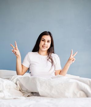 young beautiful brunette woman sitting awake in bed showing peace sign with her hands
