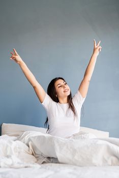 young beautiful brunette woman sitting awake in bed showing peace sign with her hands