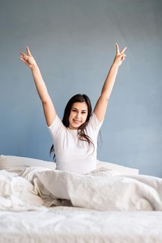 young beautiful brunette woman sitting awake in bed showing peace sign with her hands