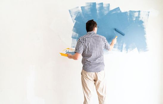 Home repair and improvement. Man coloring wall blue with a roller