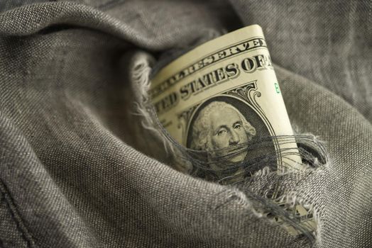 Dollar bill viewed through a hole in torn grey fabric with focus to the portrait of Washington in a federal budget hole or economic concept