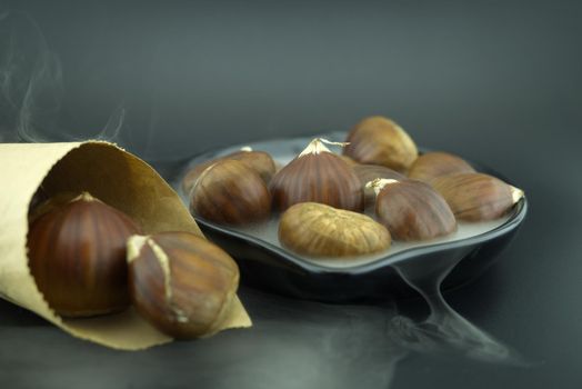 Roasting chestnuts in a black pan, surrounded by white smoke and a cone-shaped paper cone, a dish for a traditional healthy winter snack or appetizer