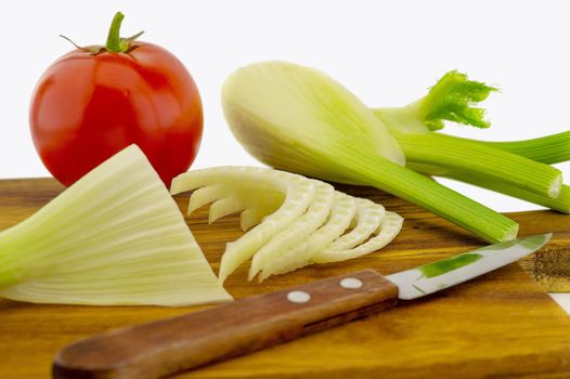 Preparing red tomato and fresh fennel slicing them on a wooden cutting board over a white background in a healthy diet and nutrition concept