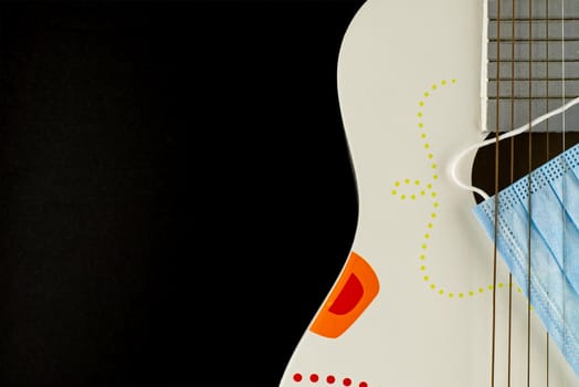 Wooden acoustic guitar body and a face mask between the strings over a black background with free space for text