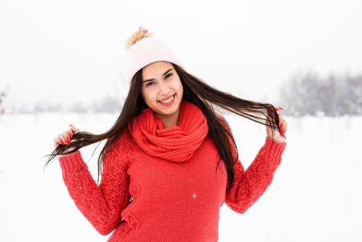 Winter season. Portrait of a beautiful smiling woman in red sweater and hat in snowy park
