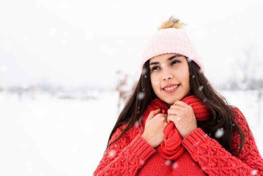 Winter season. Portrait of a beautiful smiling woman in red sweater and hat in snowy park